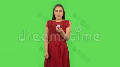 一个穿着红色连衣裙的小女孩正在打开一个小盒子，里面装着一个惊喜，她对自己看到的东西非常失望。绿色屏幕