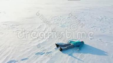 一个女孩在森林的空地上做一个雪天使的身影。 一个女孩躺在雪地里的空中摄影。