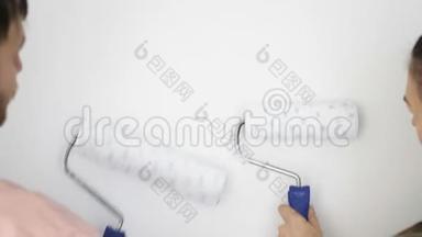 男人和女人用滚筒油漆墙壁。 在白色墙壁的背景上快乐的一对。