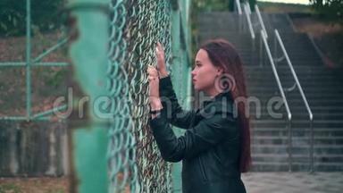 漂亮而热情的女孩穿着铁栅栏后面的自行车夹克。 被关在<strong>监狱</strong>里的年轻女子锁着金属栅栏。