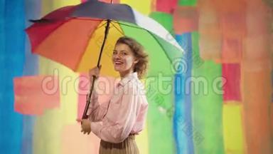 开朗的白种人年轻女子带着彩虹伞，在彩色演播室的背景下玩得很开心。 积极向上的青年