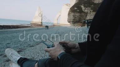 近距离男子操作无人机与遥控器坐在海滩附近著名的白海悬崖埃特雷特慢动作。