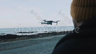 特写镜头戴帽子的人正在遥控无人机，在华丽平静的海边观看缓慢的飞行。