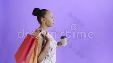 带着<strong>购</strong>物袋的非裔美国女人正在工作室里喝<strong>紫色</strong>背景的咖啡。 带花的白色裙子
