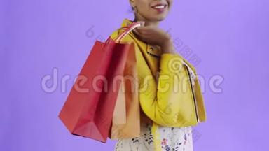 美国黑人妇女在工作室的紫色背景上带购物袋的肖像。 幸福的女人手里拿着