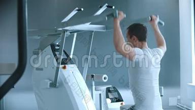 现代健身房-一个男人坐在训练器械上，在白色现代健身房训练他的手