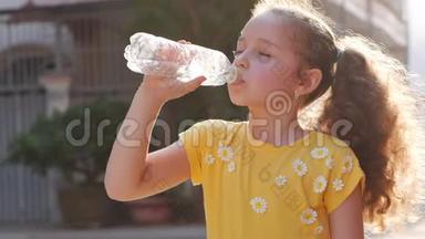 可爱的女孩解渴，从房子附近的街道上的一个塑料瓶里喝。 慢动作小女孩急切地