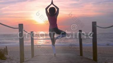 女子在木制沙滩步道练习瑜伽，美丽的夏日日落