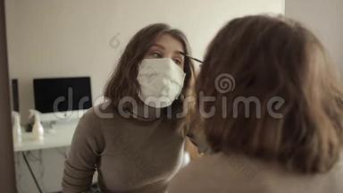 戴着防护面罩的年轻女孩在家中被隔离时在镜子前化妆。 冠状病毒。 COVID