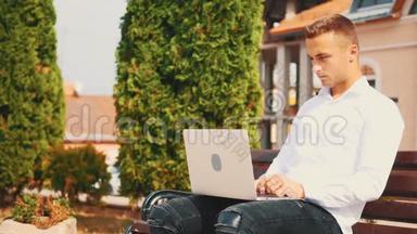 专心致志的男人，穿着商业风格，坐在公园里的户外，在笔记本电脑上打字