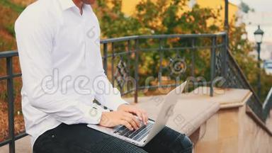 无法辨认的男人，穿着<strong>商业风</strong>格，坐在公园外面的时候，在笔记本电脑上打字