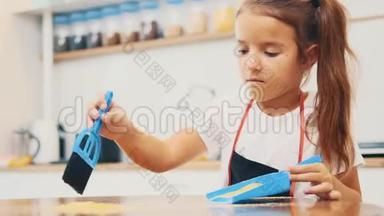 一个穿深色迪基的小漂亮女孩用蓝色的扫把和铲子清洁厨房的桌子。 失去理智。 作物。 4K.