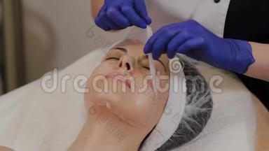 <strong>专业美容师</strong>从女人的脸上取出透明`织物抗衰老面膜。
