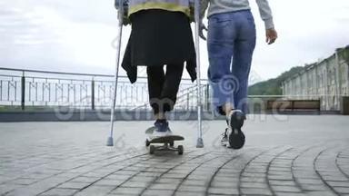 一条腿<strong>拄着拐杖</strong>的年轻人骑<strong>着</strong>滑板和他的女朋友一起散步。 残疾人的积极生活.. 这就是