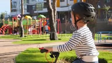 在大型<strong>儿童游乐场</strong>旁边的公园里，小男孩骑着自行车戴着防护头盔的特写4k<strong>视频</strong>