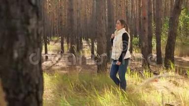 4k视频美丽的微笑女子徒步旅行背包在秋天的森林和看生<strong>长高</strong>杉树