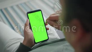 一个人<strong>独自</strong>坐<strong>在家</strong>里，一个人拿着绿色屏幕色度键智能手机