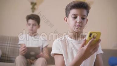 白种人男孩使用智能手机作为他的孪生<strong>兄弟</strong>坐在背景与平板电脑。 小<strong>兄弟</strong>