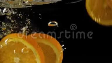 新鲜的橙片在黑色背景下随着飞溅和气泡落入水中