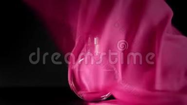 椭圆形表面的一瓶粉红色香水或精油在桌子上的粉红色布下。 粉红色的织物突然飘散
