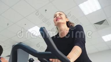 <strong>微</strong>笑的女人在健身房的自行车<strong>课</strong>上训练室内自行车。 健身训练低角度旋转自行车快乐女人