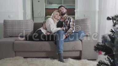 快乐白种人夫妻坐在沙发上拥抱的肖像。 恋爱中的情侣周末一起在
