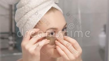 一张美丽的年轻女子的肖像，穿着浴袍和毛巾站在浴室里，在她的眼睛下敲击着<strong>补水</strong>补丁