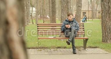 大胡子坐在秋天的公园里，用他的手机进行社交网络，滑动和滚动。 社会网络平台