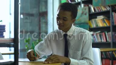 勤奋的非裔美国男学生在笔记本上做作业，在摄像机上微笑