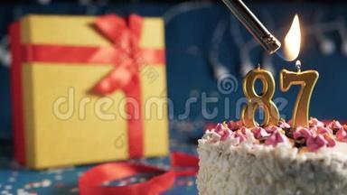 白色生日蛋糕，87号金色蜡烛用打火机点燃，蓝色背景灯和礼品黄色盒子用红色系着