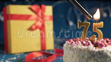 白色生日蛋糕，75根金色蜡烛，用打火机点燃，蓝色背景，黄色礼品盒用红色系着