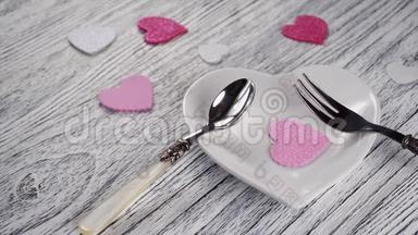 装饰的心落<strong>在心</strong>形盘子上，上面有甜点叉子和勺子。 在木质轻盈质感的桌子上.. 粉红色和白色