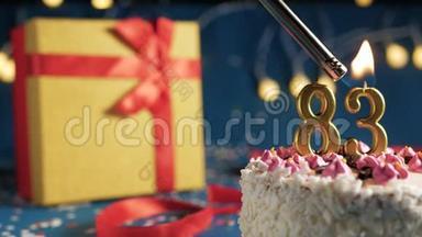白色生日蛋糕，83个金烛，用打火机点燃，蓝色背景，黄色礼品盒用红色系着