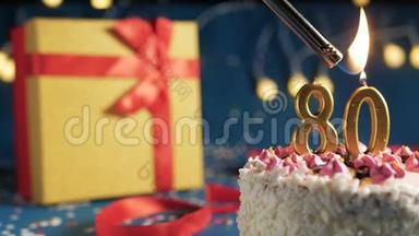 白色生日蛋糕数字80金蜡烛用打火机点燃，蓝色背景灯和礼品黄色盒子用<strong>红色系</strong>起来