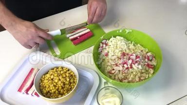 男人做沙拉。 切片蟹棒在切割板上。 容器旁边是碎北京白菜.. 玉米和蛋黄酱