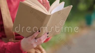 年轻迷人的红头发女人，戴着帽子和毛衣，在自然公园的长凳上看书。 秋天凉爽的一天。