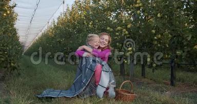 母女俩坐在苹果园里拥抱着，微笑着，4k