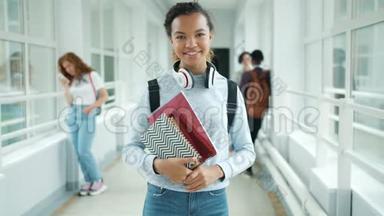 快乐的混血少年捧着书站在大学走廊微笑