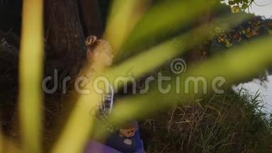 荷花中的年轻女子摆姿势，在夏日森林里冥想户外瑜伽.. 在河边练习瑜伽冥想的女孩