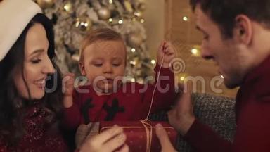 <strong>亲近</strong>快乐的白种人父母帮助他们的孩子打开礼物盒，穿在冬天的毛衣坐在舒适