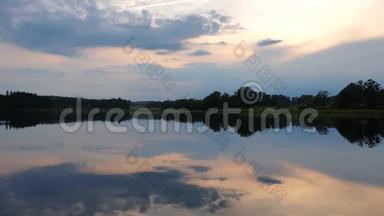 在平静的夏夜欣赏绚丽的日落。 湖岸有绿树和植物在晶莹洁净的镜面水中倒影..