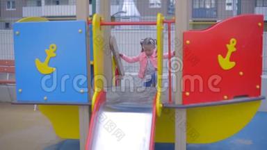 穿牛仔裤的金发小女孩在儿童公园`玩耍。