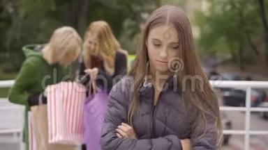 年轻悲伤的女人羡慕前景，而她的两个美丽的金发女朋友站在街上展示她的前景