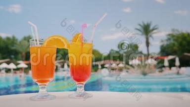 池和棕榈树的背景上，两杯清凉的鸡尾酒立在桌上.. 天堂和豪华度假胜地