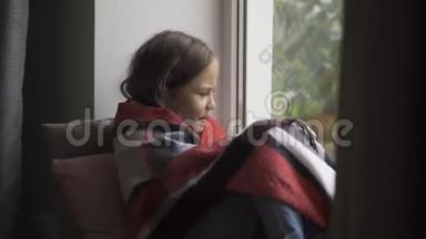 生病的白种人女孩被毯子覆盖坐在窗台上在家里。 孩子发烧了，她感冒了。 概念