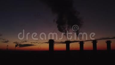 夕阳和城市背景下高高的烟囱。 浓烟高高升起. 五座冷却塔的剪影