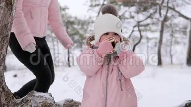 穿着粉红色冬季连衣裙的小女孩在雪天上雪橇后吃圣诞姜饼。 可爱的家庭过冬