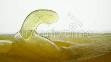 金色液体，表面有气泡和空气滴。 玉米油与油一起倒入透明