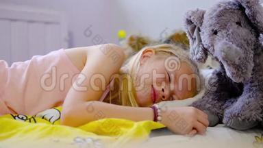 一个漂亮的金发女孩穿着粉红色睡衣，一大早就睡在床上，床上铺着黄色的床上用品。 女孩和她