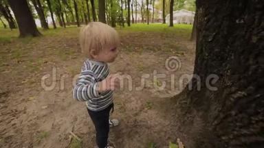 漂亮的小男孩走在靠近一棵树的公园里。